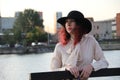 Portrait of a woman with red hair and a classic black hat by the city river Royalty Free Stock Photo