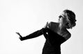 Portrait of woman with short curly blonde hair in black dress is defending from something coming from below on white Royalty Free Stock Photo