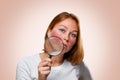 Portrait of a woman showing redness on her cheeks, through a magnifying glass. Pink background. The concept of rosacea Royalty Free Stock Photo