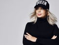 Portrait of woman with straight long blonde hair in black cap and sweater standing with hands crossed in front of her Royalty Free Stock Photo