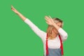 Portrait of woman in stylish denim overalls raising hands in dab dance pose, celebrating success Royalty Free Stock Photo