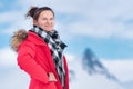 Portrait of woman traveler dressed in red winter jacket, scarf on background of mountains, blue sky with clouds