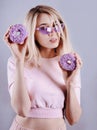 Portrait of a woman in trendy sunglasses with violet donuts in hands