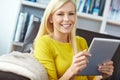 Portrait of a woman using a tablet while sitting on a sofa. Happy young female watching and browsing online on her Royalty Free Stock Photo
