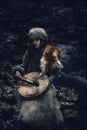 Portrait of a woman wearing fur hat and fox fur pelt on her shoulders.Playing shamanic drum.Shot in forest surroundings. Royalty Free Stock Photo