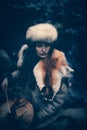 Portrait of a woman wearing fur hat and fox fur pelt on her shoulders.Playing shamanic drum in the forest. Royalty Free Stock Photo