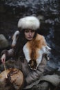 Portrait of a woman wearing fur hat and fox fur pelt on her shoulders.Playing shamanic drum in the forest. Royalty Free Stock Photo