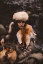 Portrait of a woman wearing fur hat and fox fur pelt on her shoulders.Playing shamanic drum in the forest. Royalty Free Stock Photo