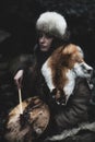 Portrait of a woman wearing fur hat and fox fur pelt on her shoulders.Playing shamanic drum in the forest. Royalty Free Stock Photo