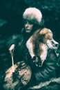 Portrait of a woman wearing fur hat and fox fur pelt on her shoulders.Playing shamanic drum in the forest. Royalty Free Stock Photo