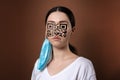 Portrait of a woman wearing protective mask with a QR code instead of a face. Brown background. The concept of