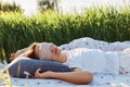 Portrait of woman wearing sleeping mask and white t shirt lying on soft bed in the middle of green field or meadow, female sleeps Royalty Free Stock Photo