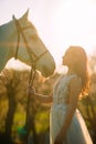 Portrait of woman in white dress near horse at sunset