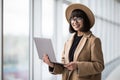 Portrait of young woman working holding laptop standing against panoramic window with city view Royalty Free Stock Photo