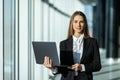 Portrait of young woman working holding laptop standing against panoramic window with city view Royalty Free Stock Photo