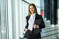 Portrait of young woman working holding laptop standing against panoramic window with city view Royalty Free Stock Photo