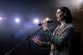 Portrait of women speaking through a microphone in dark conference hall. woman talks into microphones at press Royalty Free Stock Photo