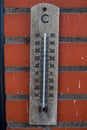 A portrait of a wooden mercury thermometer indicating the outdoor temperature in degrees celcius and is hanging on a red brick