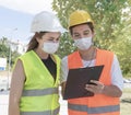 Portrait of worker and engineer wearing face masks checking production process and discussing project details on construction site Royalty Free Stock Photo