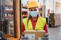 Portrait of worker woman holding cardboard box inside warehouse while wearing safety mask - Focus on face Royalty Free Stock Photo