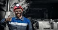 Portrait working young male miner in red cap showing thumbs up, excellent sign background coal mine. Industrial concept