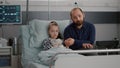 Portrait of worried father holding hospitalized sick daughter hand looking into camera