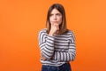 Portrait of worried frustrated woman with brown hair in long sleeve striped shirt. indoor studio shot on orange