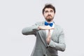 Portrait of worried handsome bearded man in casual grey suit and blue bow tie standing with timeout gesture hands and looking at Royalty Free Stock Photo