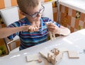 Portrait of a 7-8 year old boy with a screwdriver, carefully assembling a wooden car, sitting at the kitchen table Royalty Free Stock Photo