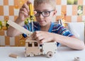 Portrait of a 7-8 year old boy with a screwdriver, carefully assembling a wooden car, sitting at the kitchen table Royalty Free Stock Photo