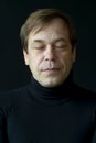 Portrait of a 45-50-year-old man with his eyes closed in a golf sweater on a dark background.