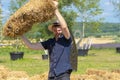 Portrait of a 35-40-year-old man in a straw hat holding a bale of straw over his head against a background of blue sky and clouds. Royalty Free Stock Photo