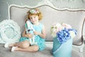 Portrait of 5 years old curly blonde smiling girl in blue dress and wreath sitting on sofa with rabbit toy in hands. Waiting for Royalty Free Stock Photo