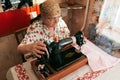 Portrait of 70 years old senior woman in spectacles using sewing machine, working from home. Work for old aged people, clothing an Royalty Free Stock Photo