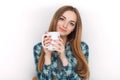 Portrait of a young adorable blonde woman in blue plaid shirt enjoying her warm cozy drink in big blank white mug. Royalty Free Stock Photo