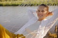 Portrait of young adult attractive european woman wearing white shirt sitting in hammock on the bank of the river, looking at Royalty Free Stock Photo