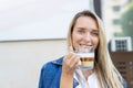 Portrait of young adult attractive happy woman enjoy smiling and hold cup drinking hot cappuccino coffee against street Royalty Free Stock Photo