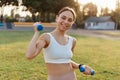 Portrait of young adult attractive smiling woman, being happy to workout in stadium outdoor, holding blue dumbbells in hands, Royalty Free Stock Photo