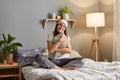 Portrait of young adult attractive woman sitting on bed hugging pillow in modern light interior bedroom in her apartment, wearing Royalty Free Stock Photo