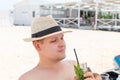 Portrait of young adult caucasian man wearing hat enjoy having fun drinking fresh mojito cocktail and sunbathing on sand Royalty Free Stock Photo