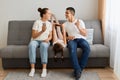 Portrait of young adult family of holding and using mobile phones while sitting on sofa. Parents and their daughters with modern