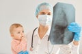 Portrait of young adult female pediatrist wearing medical uniform, holding infant baby girl, examining child`s health in clinic,