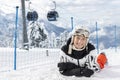 Portrait young adult happy beautiful female skier woman lying on snow with ski lift gondola and sniwcapped mountain Royalty Free Stock Photo