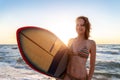 Portrait young adult slim sporty female surfer girl with surfboard silhouette stand at ocean coast wave against warm Royalty Free Stock Photo