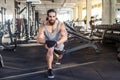 Portrait of handsome young adult sportman athlete with long curly hair working out in gym, squating on one knee, stretching after