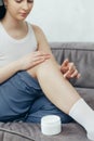 Portrait of young adult woman applying body lotion for skin on legs while sitting on couch at home Royalty Free Stock Photo