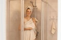 Portrait of young adult woman getting out of the shower, standing and looking at camera with happy facial expression, wrapped her Royalty Free Stock Photo