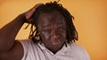 Portrait of young african american black man stroking his braided hair isolated over orange background