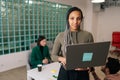 Portrait of young African American businesswoman standing in modern office holding laptop computer and smiling looking Royalty Free Stock Photo