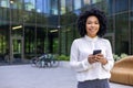 Portrait of a young African American businesswoman standing outside an office center, holding a mobile phone and smiling Royalty Free Stock Photo